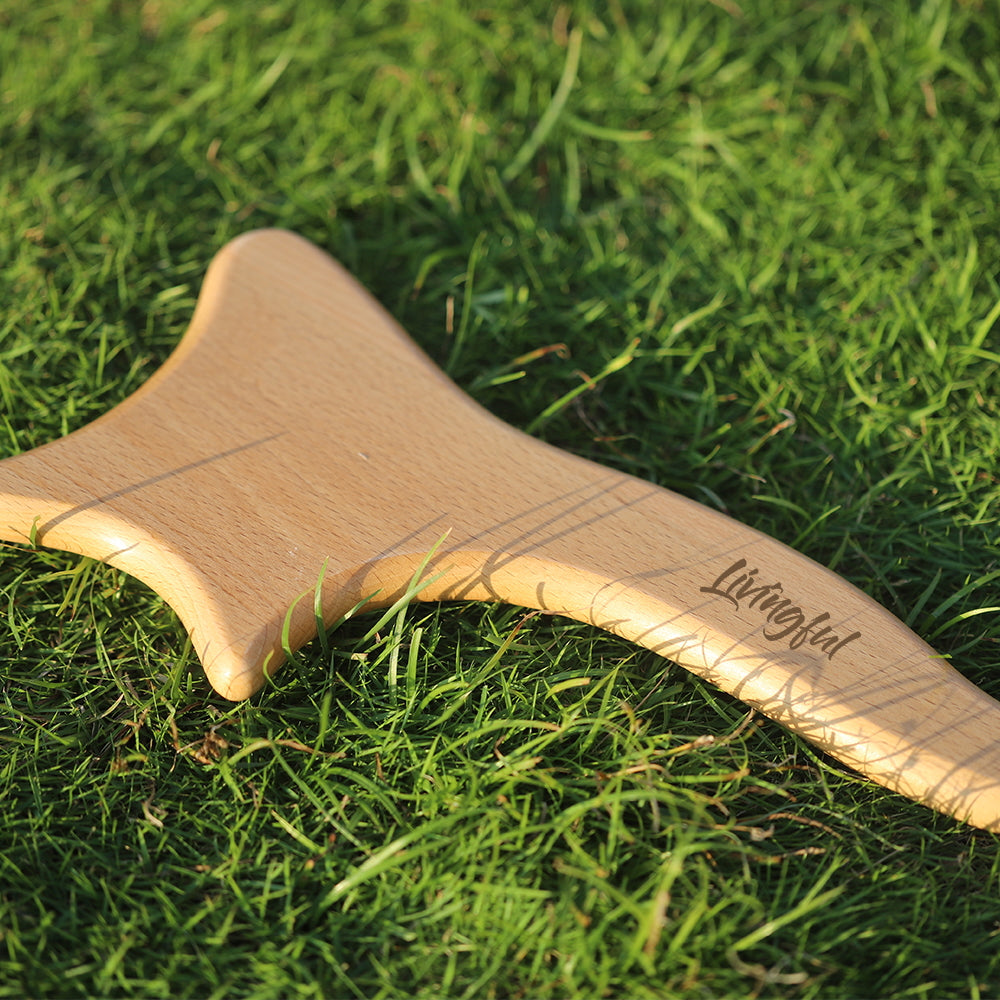 A Premium Wood Massage Tool 4 Sides from the brand "Livingful" rests on grass, resembling the curves of a Gua Sha tool.