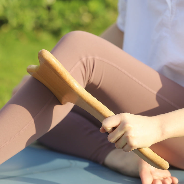 A person wearing pink leggings uses the Livingful Premium Wood Massage Tool 4 Sides on their leg outdoors, promoting lymphatic drainage.