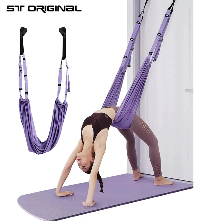 In a display of impressive yoga skills, a person uses the Aerial Yoga Strap from ST Original in purple for an inverted pose on a yoga mat next to a door, enhanced by an adjustable stretch strap.